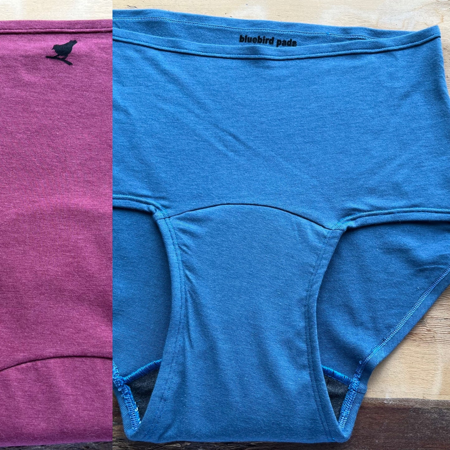 Blue underwear with 'bluebird pads' branding on a wooden surface